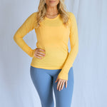 Model wearing the "breathe" long sleeve shirt from The Sweat Society. She is wearing the yellow color and looking at the camera. 