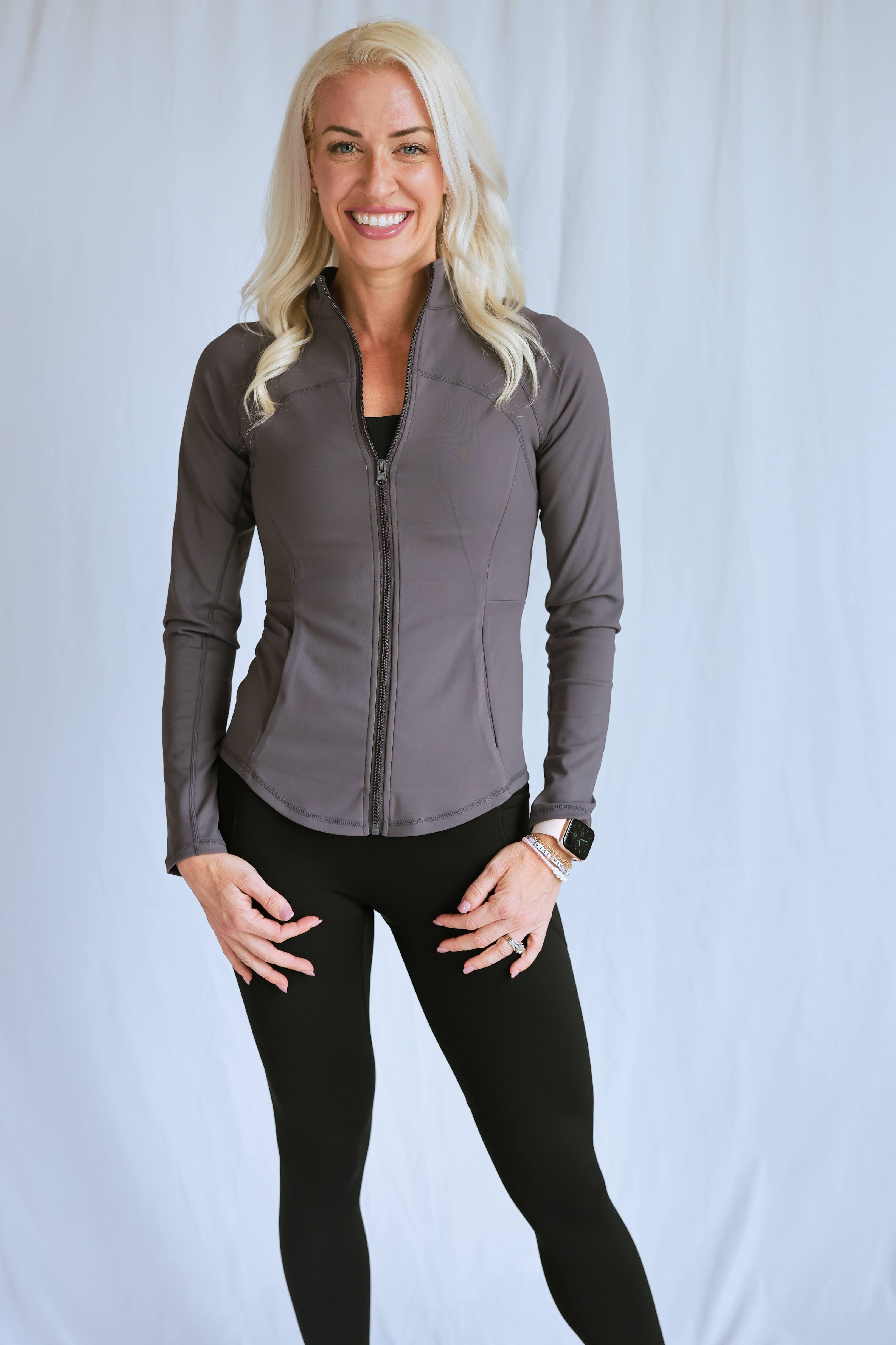 Model wearing "smooth" fitted jacket from the Sweat Society. She is wearing the grey color and smiling at the camera. 